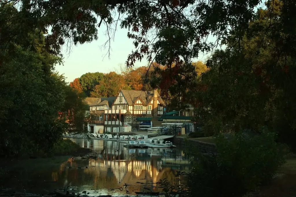 Mock-Tudor boathouses and docks reflected in the Schuylkill River under autumn trees at sunrise