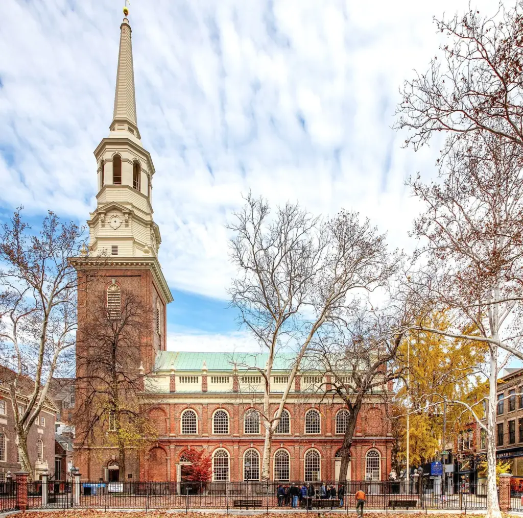 Christ Church's red brick body and tall white steeple rising above bare autumn trees