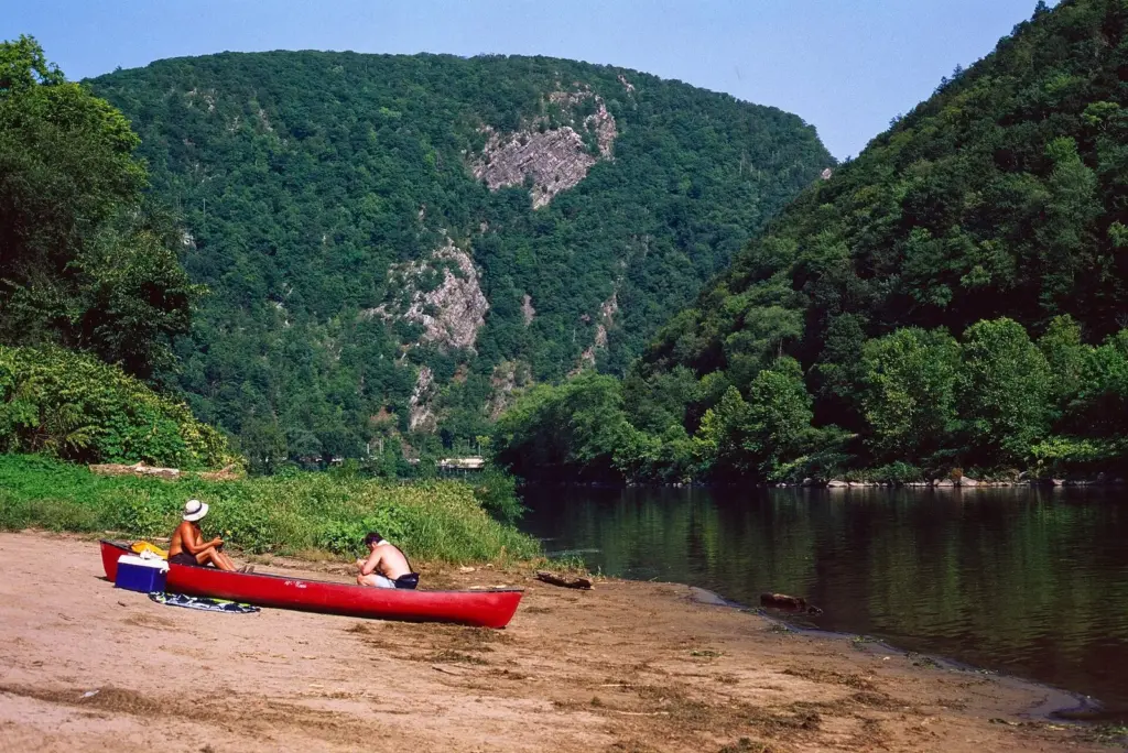 The Delaware River flowing between the forested ridges of the Delaware Water Gap, with a red canoe pulled up on a sandy bank