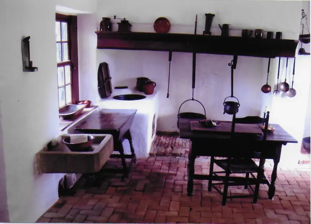 A whitewashed kitchen with a hearth, iron pots and a wooden table inside Ephrata Cloister