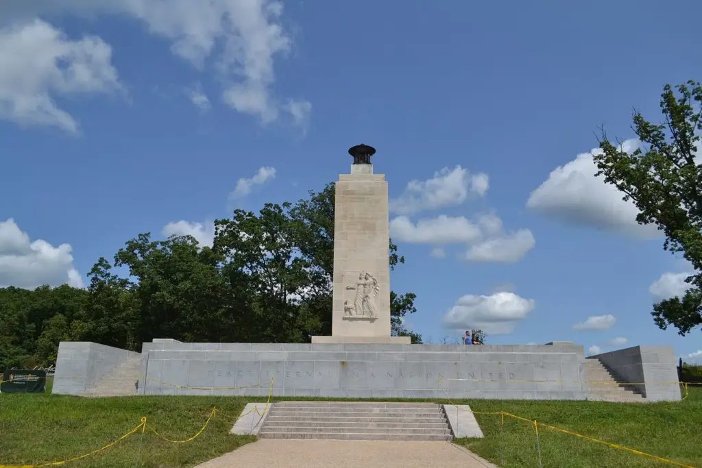 The tall stone shaft of the Eternal Light Peace Memorial on Oak Hill under a blue sky with white clouds