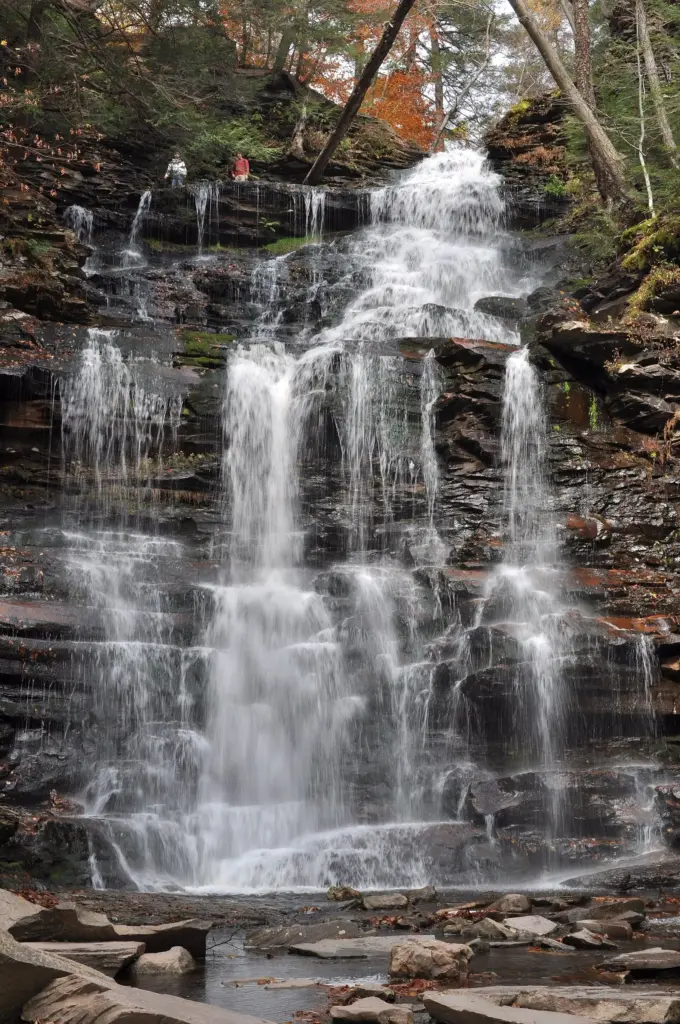 Ganoga Falls dropping over layered rock ledges in Ricketts Glen State Park, with autumn leaves on the trees around it