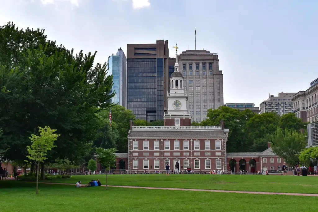 Independence Hall's red brick facade and white clock tower seen across the lawn of Independence Mall