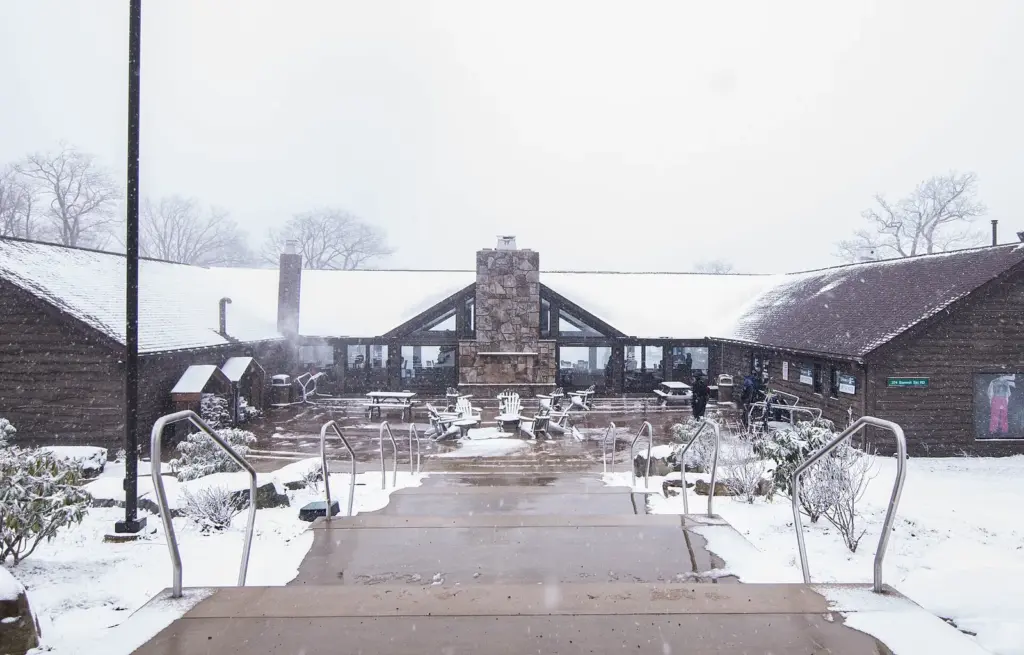 The wooden main lodge at Laurel Mountain with a stone chimney and fresh snow on the deck