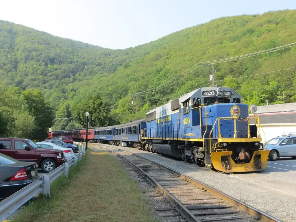 A blue diesel locomotive pulling Lehigh Gorge Scenic Railway coaches beside wooded hills in Jim Thorpe