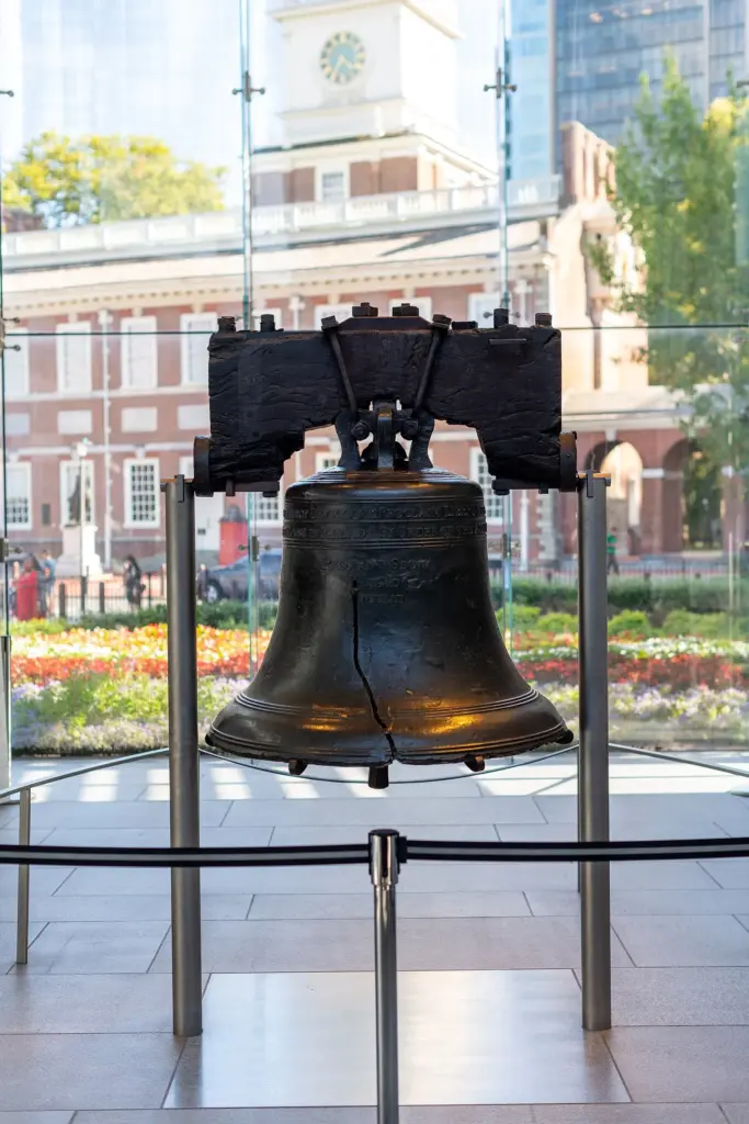 The cracked Liberty Bell hanging in its glass pavilion with Independence Hall visible through the window behind