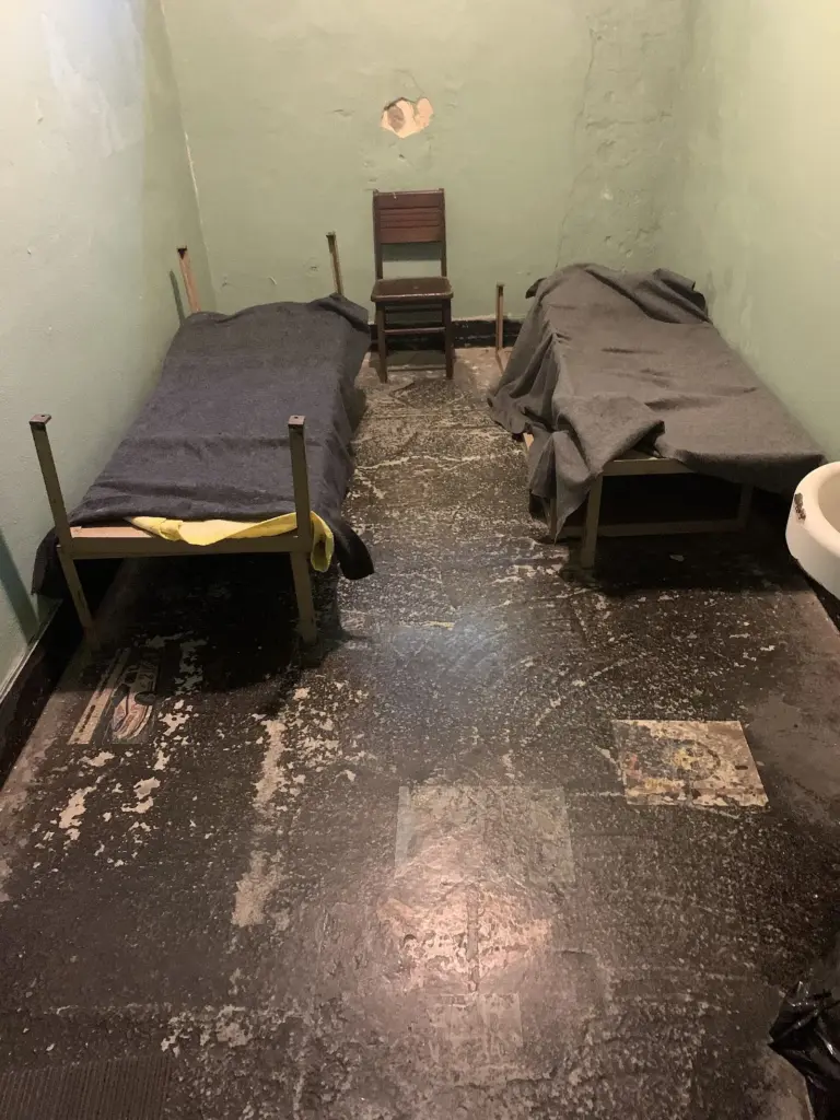 A small jail cell with two bunks and a worn floor at the Old Jail Museum