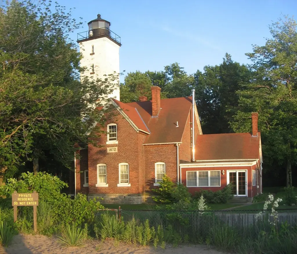 The white tower and red brick keeper's house of Presque Isle Lighthouse among summer trees