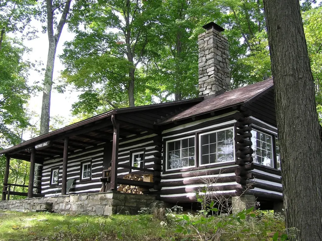 A rustic Civilian Conservation Corps log lodge with a stone chimney among tall trees at Promised Land State Park