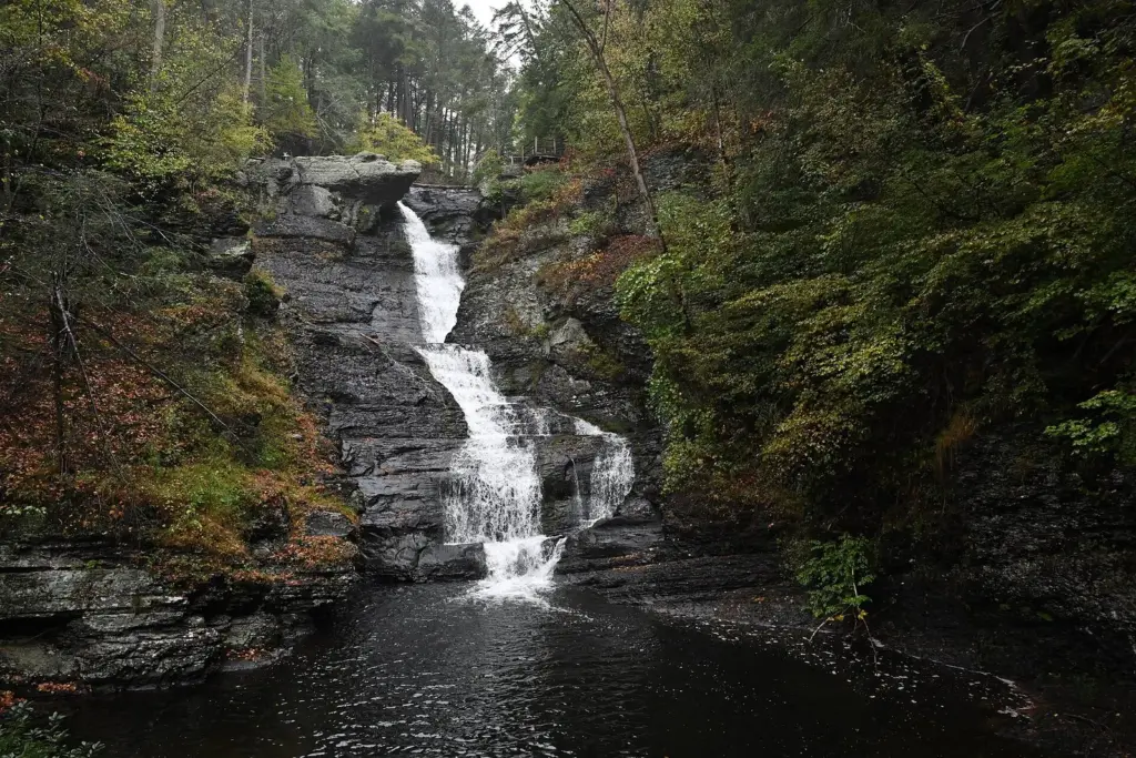 Raymondskill Falls pouring down dark rock ledges into a pool, framed by late-September forest