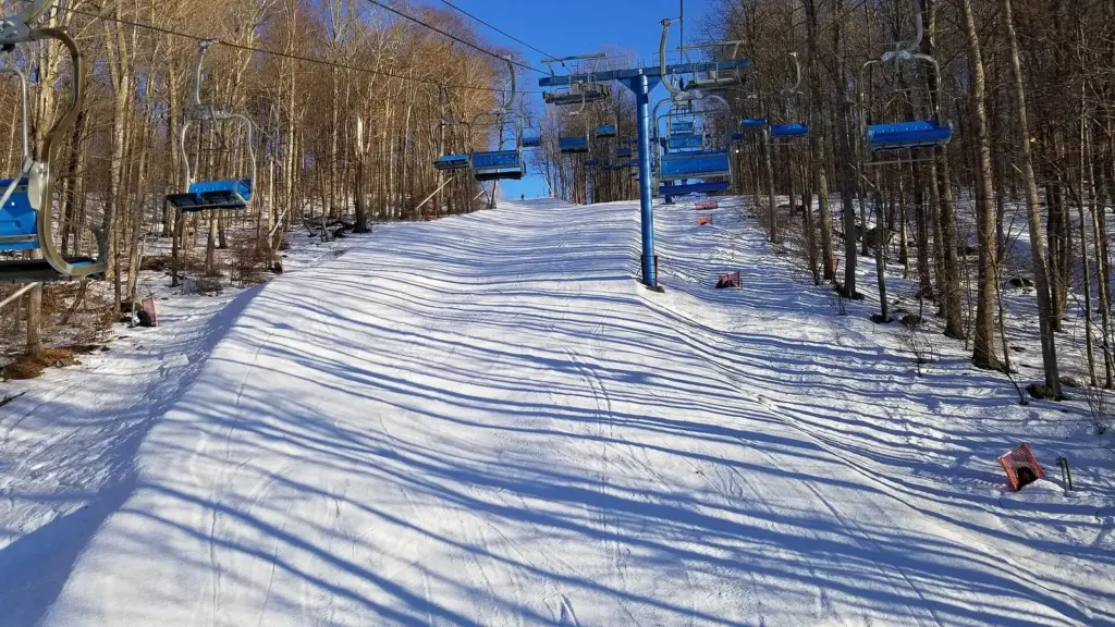 Blue chairlifts rising over a groomed trail through bare winter woods at Shawnee Mountain