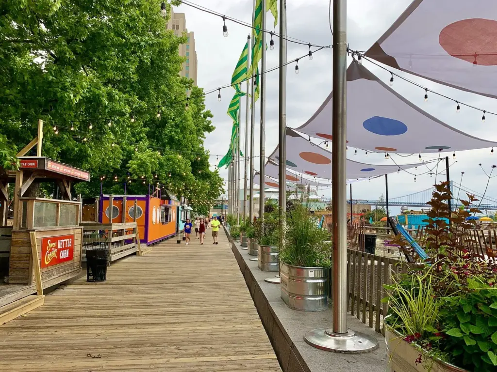Boardwalk with string lights and shade sails along the river at Spruce Street Harbor Park