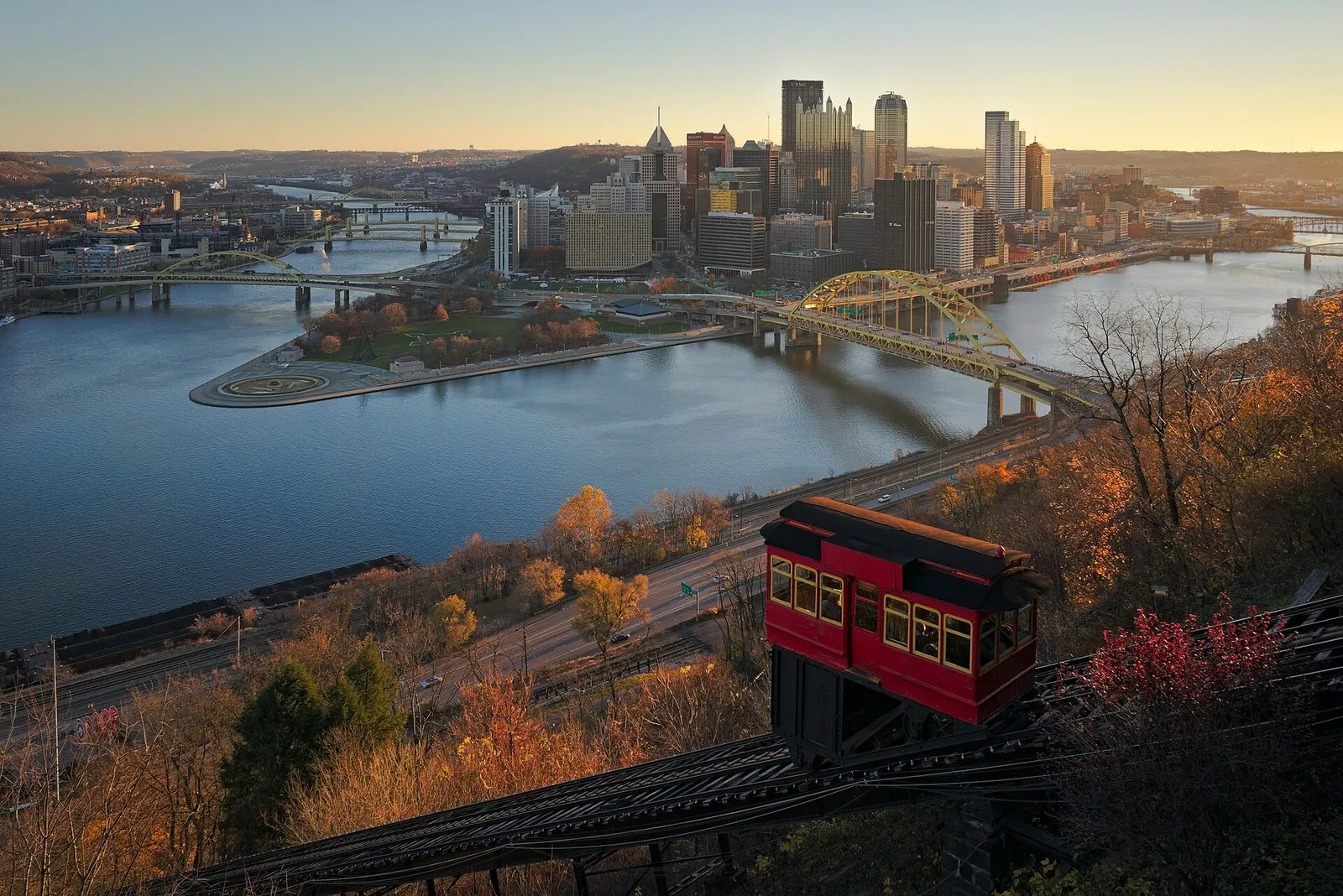 A red Duquesne Incline car climbing above the rivers and downtown Pittsburgh in autumn, one of the classic things to do in Pennsylvania