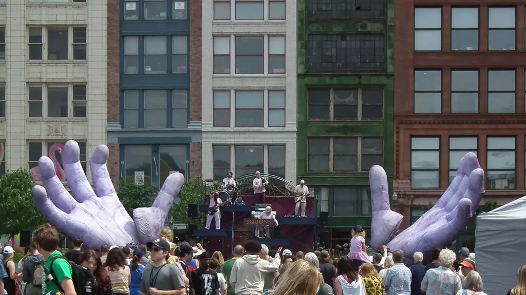 Giant inflatable purple hands rising above a performance stage and crowd in downtown Pittsburgh