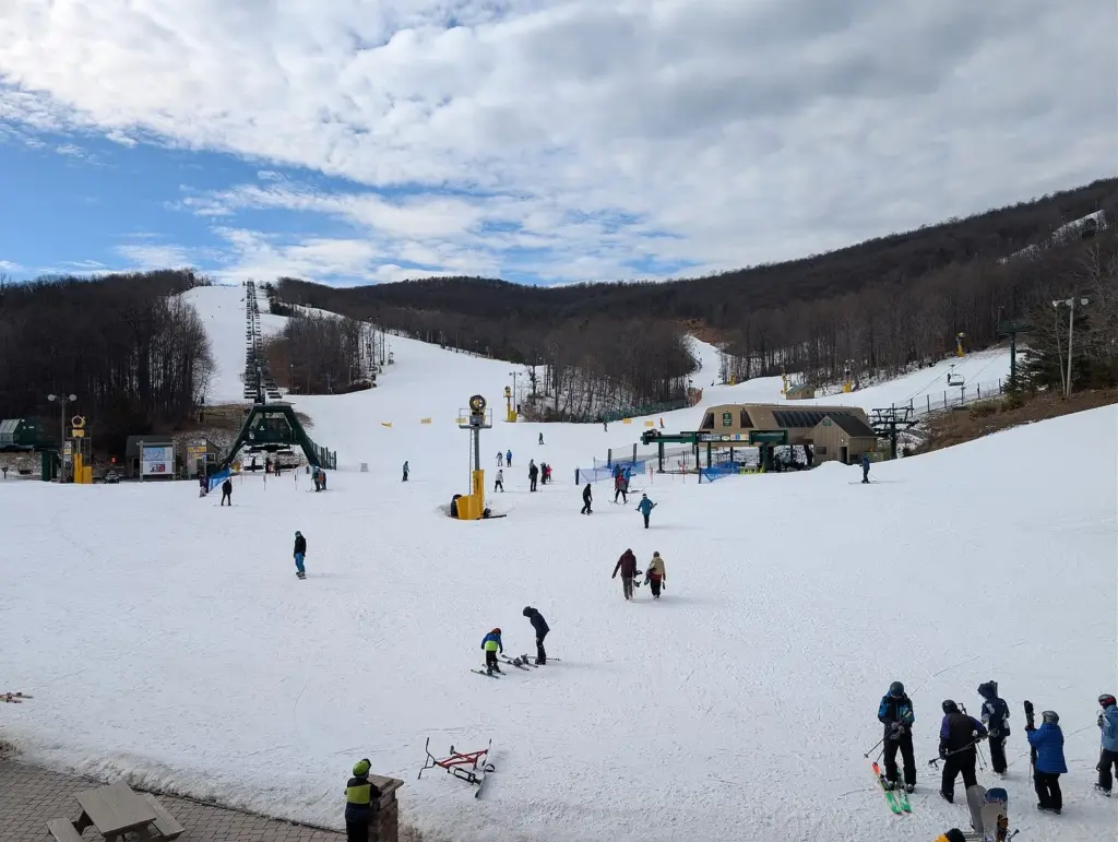 Skiers at the snowy base area of Whitetail Resort with chairlifts and wooded slopes behind