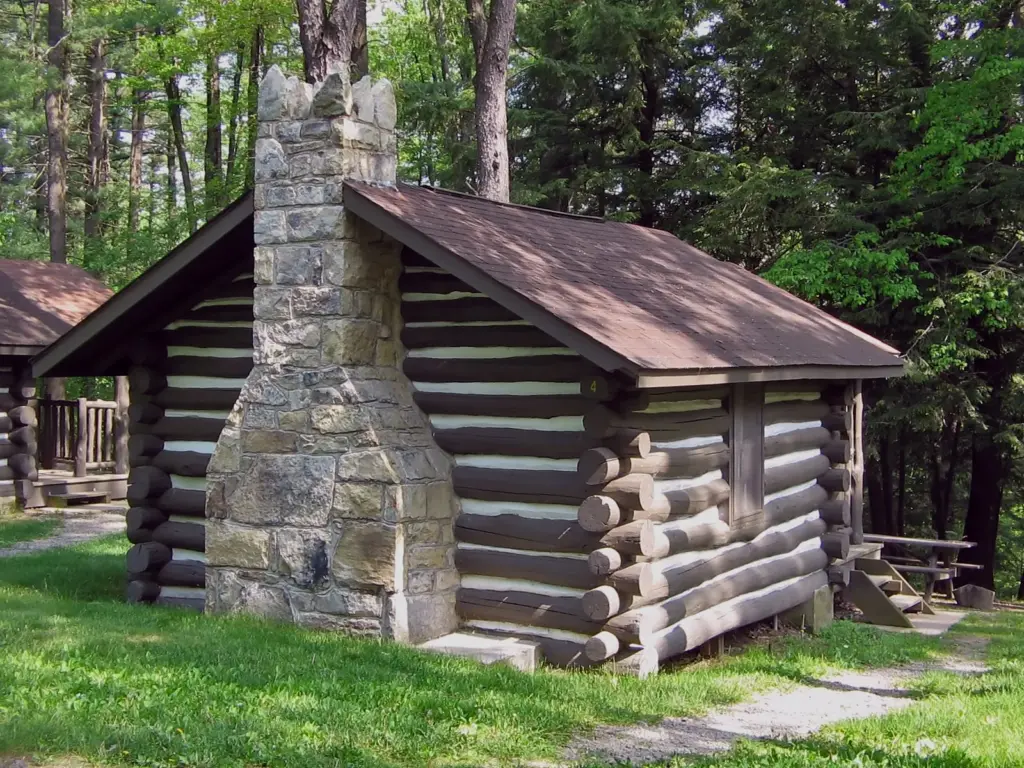 A one-room log cabin with a stone chimney among trees at Black Moshannon State Park