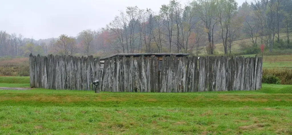 The reconstructed circular log stockade of Fort Necessity in a meadow with autumn trees behind