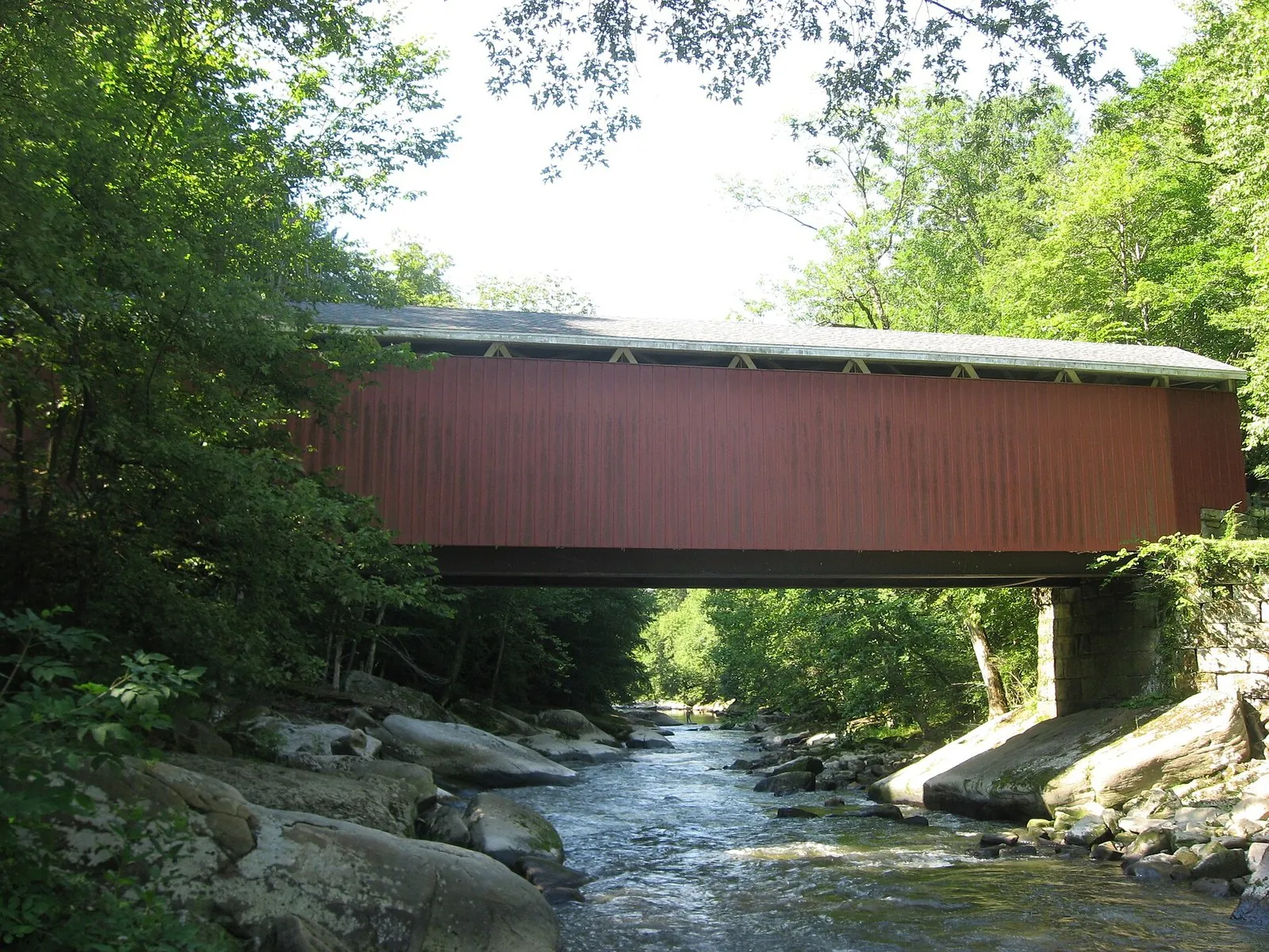 The red McConnells Mill covered bridge spanning rocky Slippery Rock Creek in spring green, one of the Pennsylvania state parks