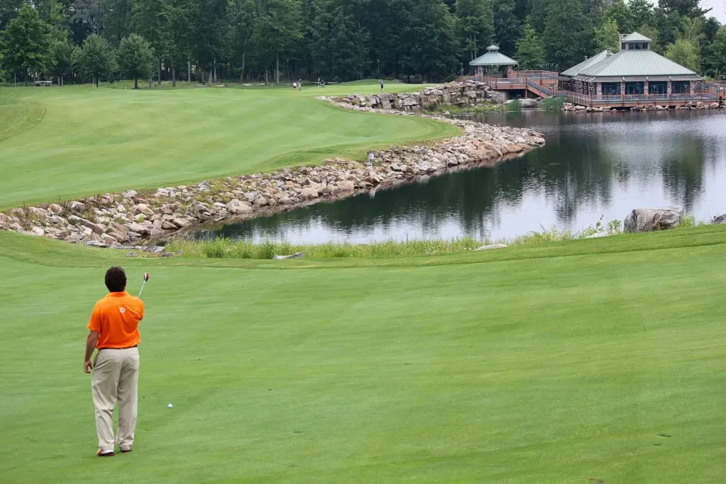 A golfer on a green fairway beside a pond and stone-edged water feature on the Mystic Rock course