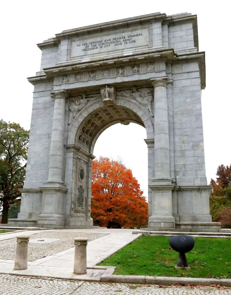 The granite National Memorial Arch at Valley Forge framed by a tree in red fall color