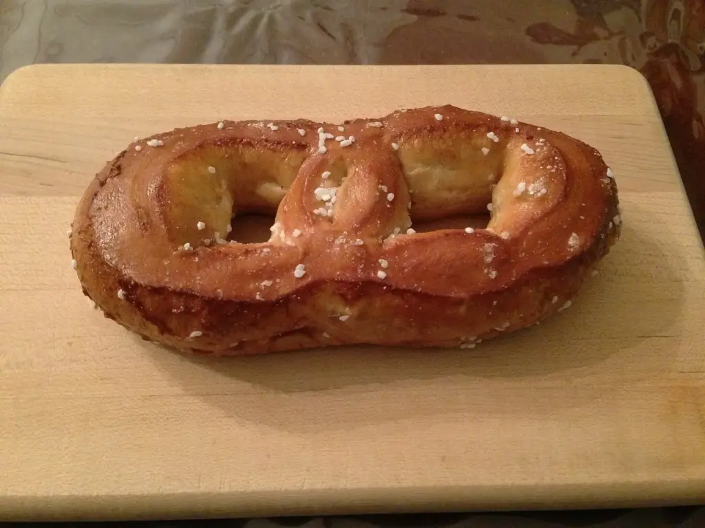 A golden Philly-style soft pretzel with coarse salt on a wooden board
