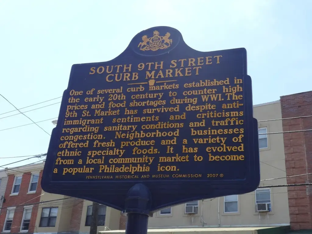 Blue Pennsylvania historical marker for the South 9th Street Curb Market against a summer sky