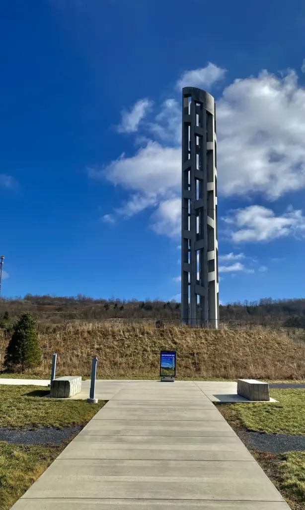 The tall concrete Tower of Voices rising above a path and meadow under a blue sky