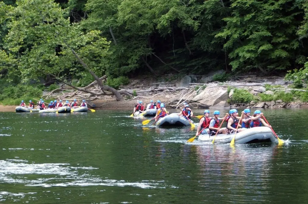 Rafters in helmets paddling inflatable rafts on the Youghiogheny River below wooded banks